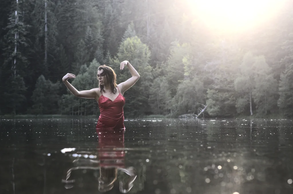 Jiulia Via en robe rouge dans un lac entouré de forêt