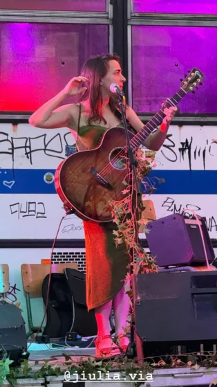 Jiulia Via en Performance Live avec Guitare Jiulia Via en concert avec sa guitare, devant un décor de graffitis et lumières colorées
